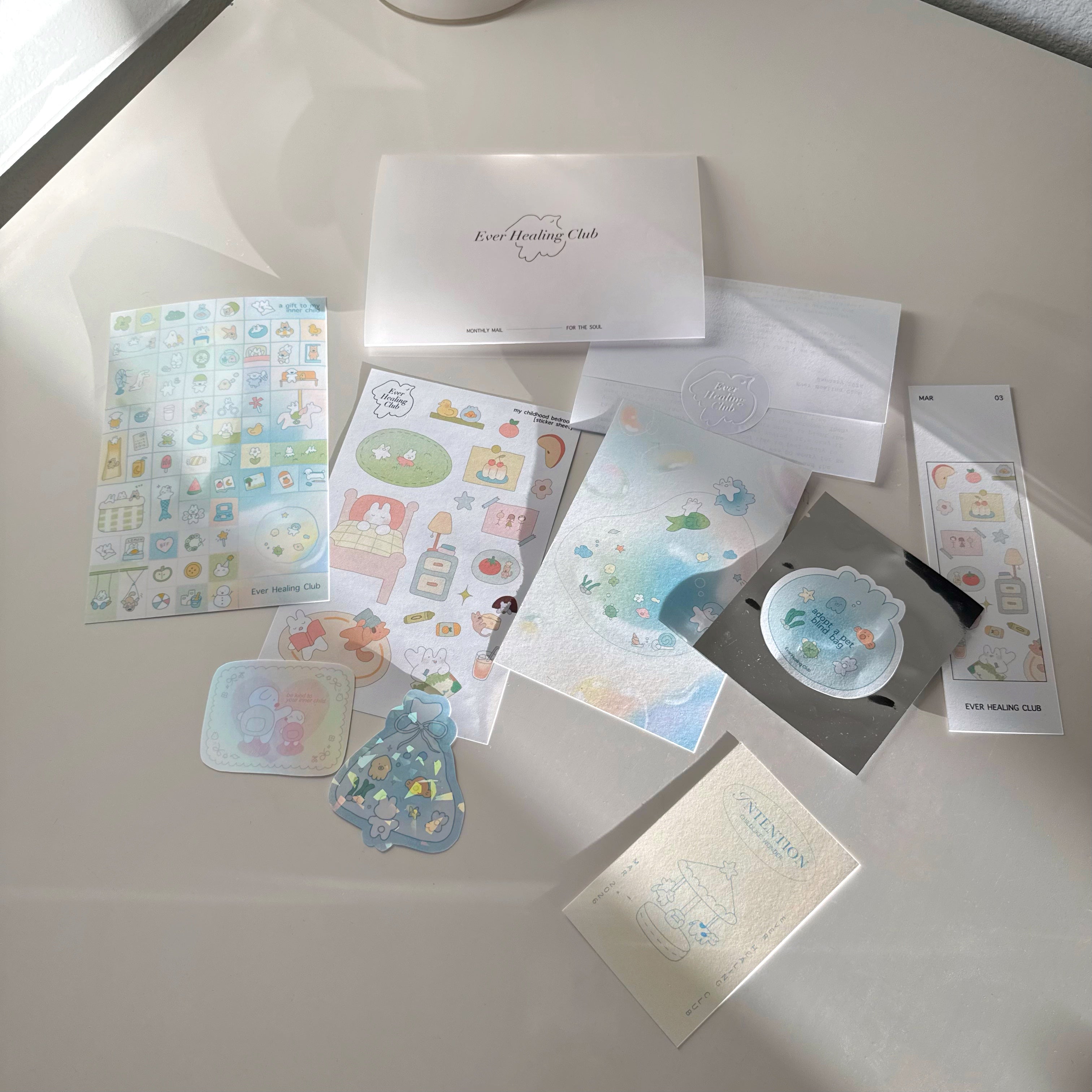 Collection of stationery items including cards, stickers, and envelopes on a light surface. Signature