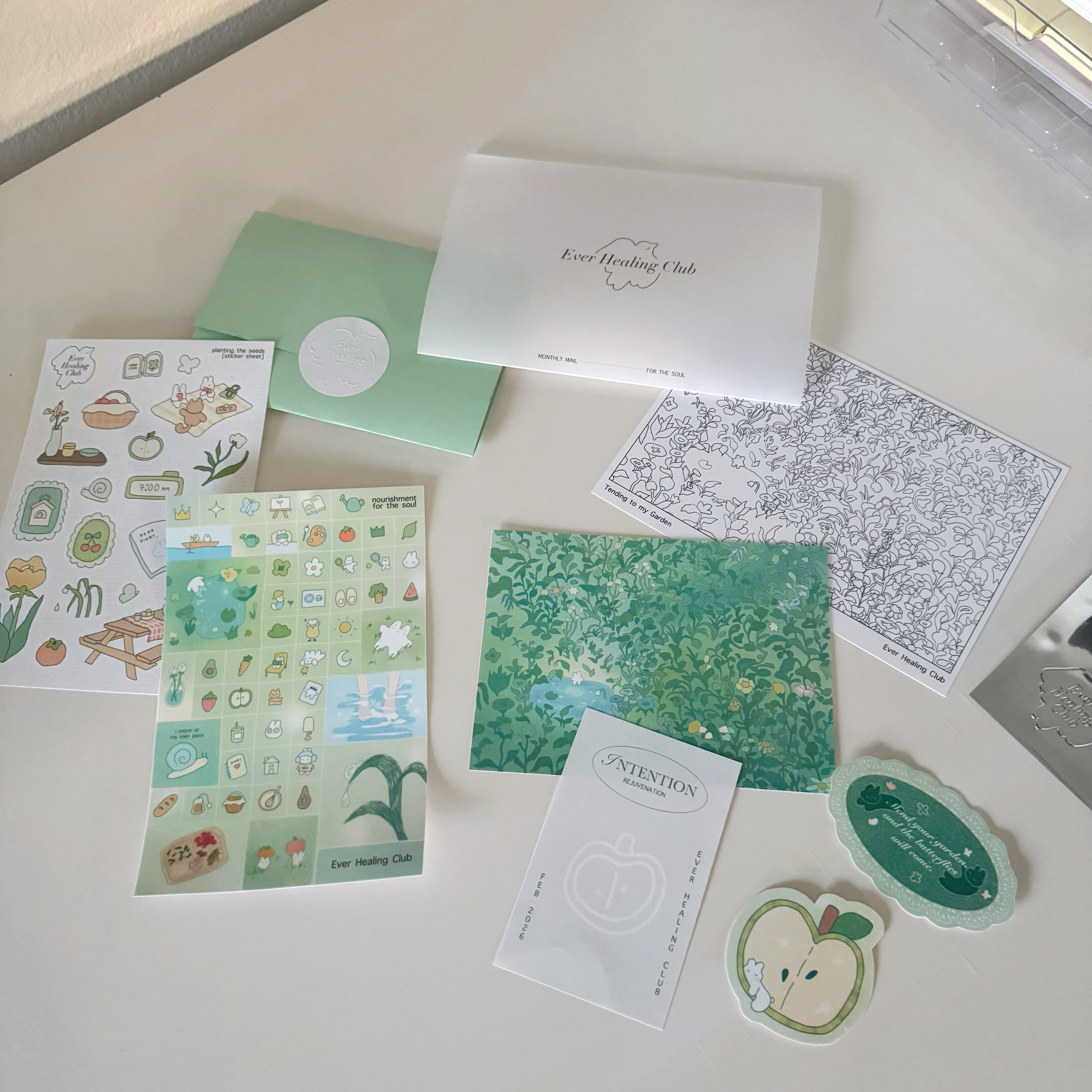 Collection of green stationery items including stickers, cards, and a box on a white surface. Signature