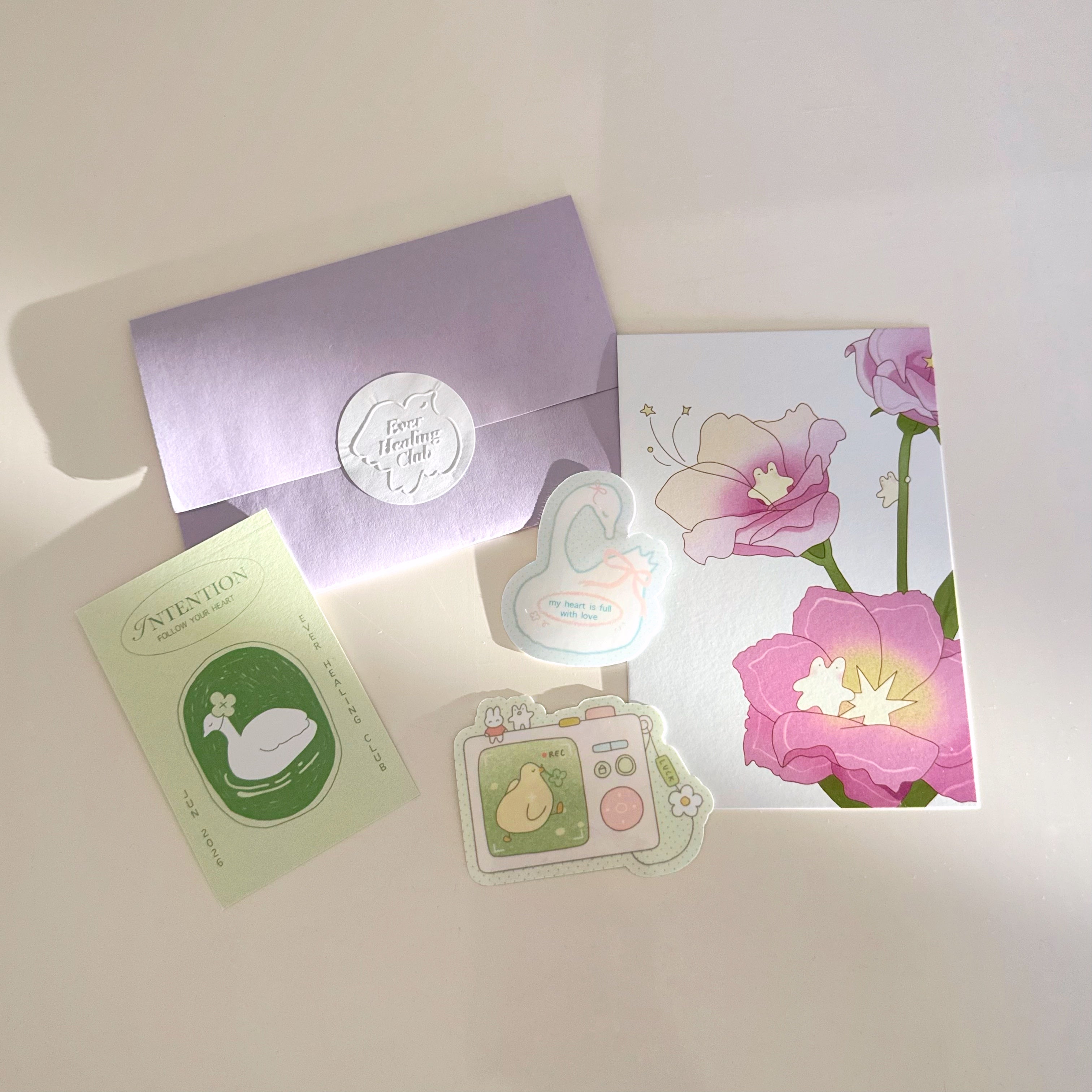 Collection of stationery items including a postcard, letter, intention card, and vinyl stickers with 'ever healing club' branding. Snail Mail